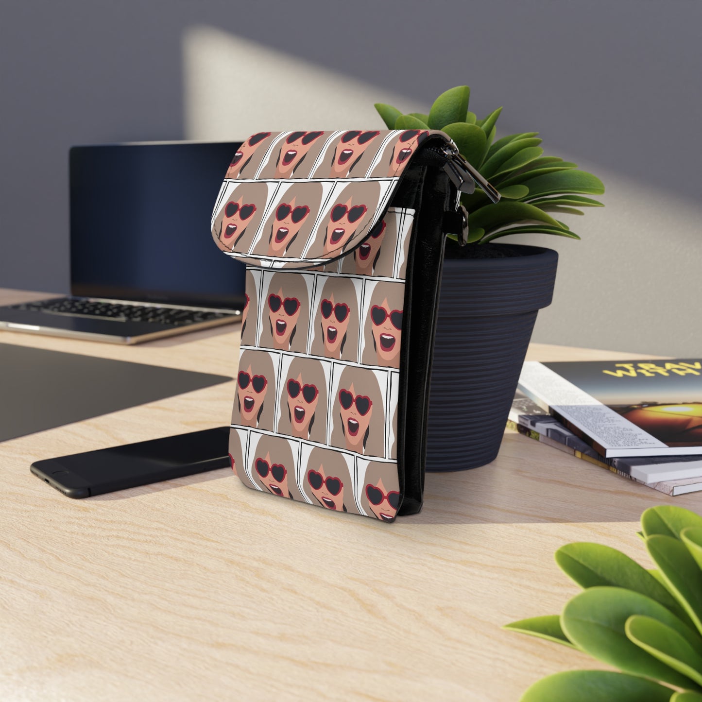 Happy Swiftie Cell Phone Wallet Bag with stylish face print standing on wooden desk near plant and laptop