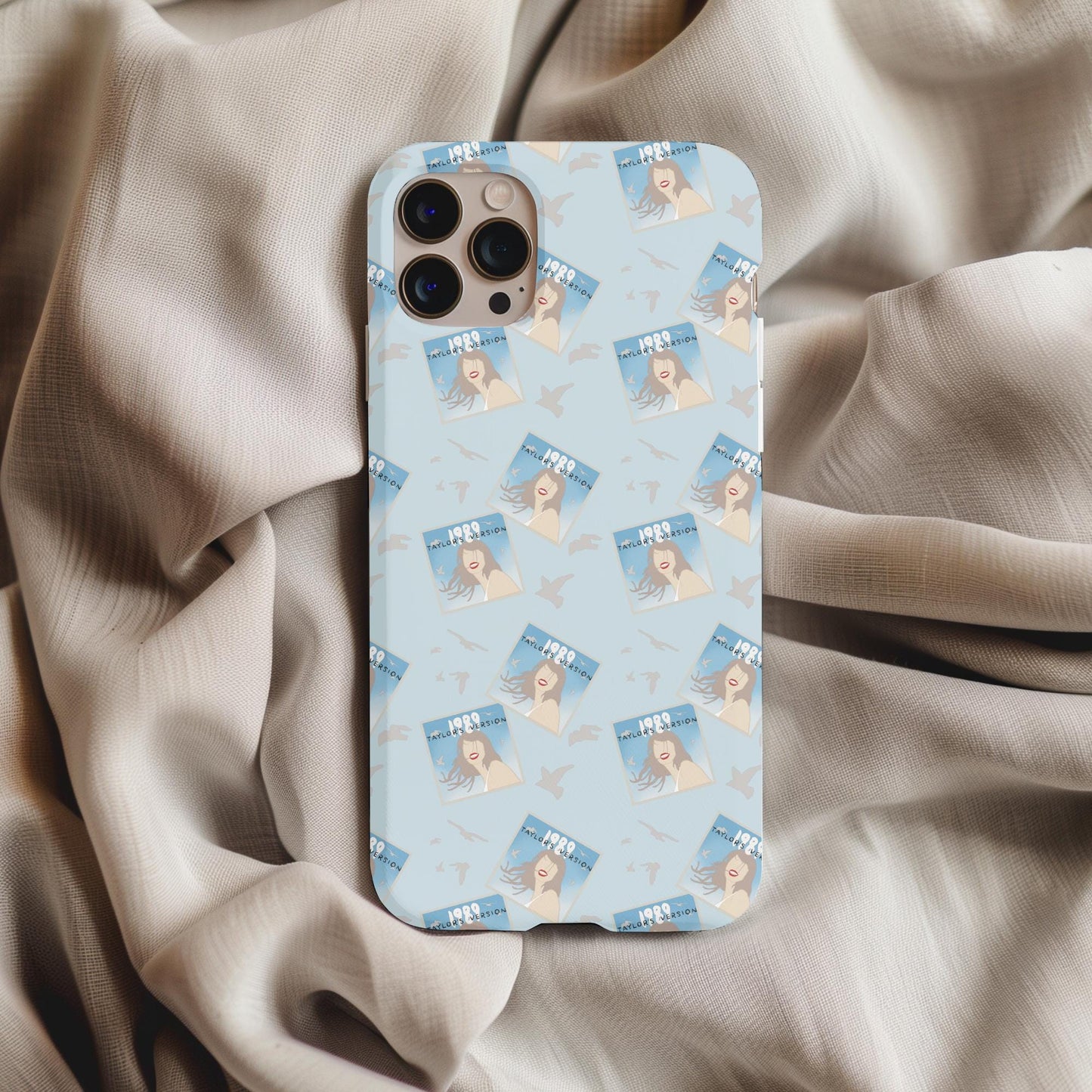 Taylor Swift 1989 Phone Case featuring album cover art pattern on a light blue background resting on beige fabric.