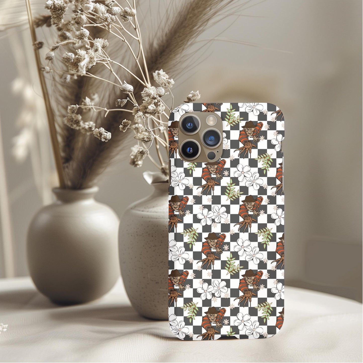 Floral Freddy Checker Phone Case with brown floral and checkerboard pattern displayed on a table with vases background