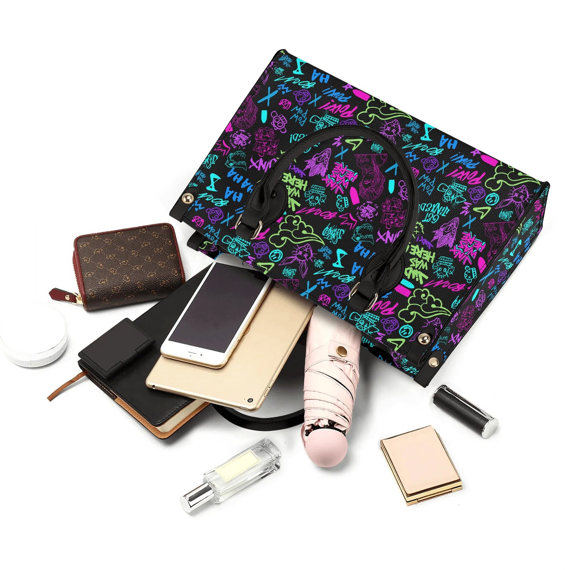 Arcane Jinx Graffiti Leather Handbag with colorful graffiti pattern and black handles displayed with personal items nearby