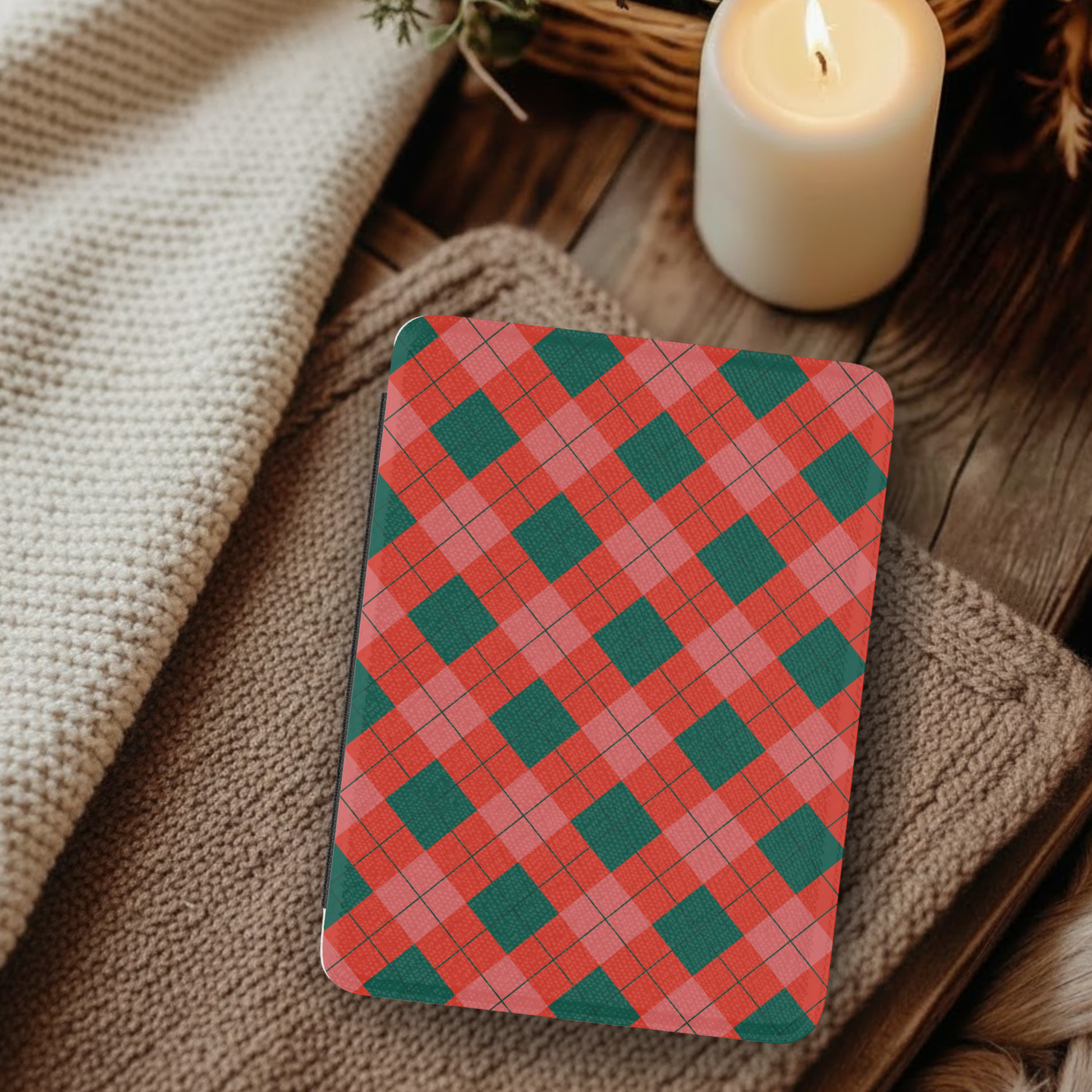 Classic Christmas Plaid Leather Kindle Case with Hand Strap resting on cozy knitted blankets beside a lit candle on wooden surface