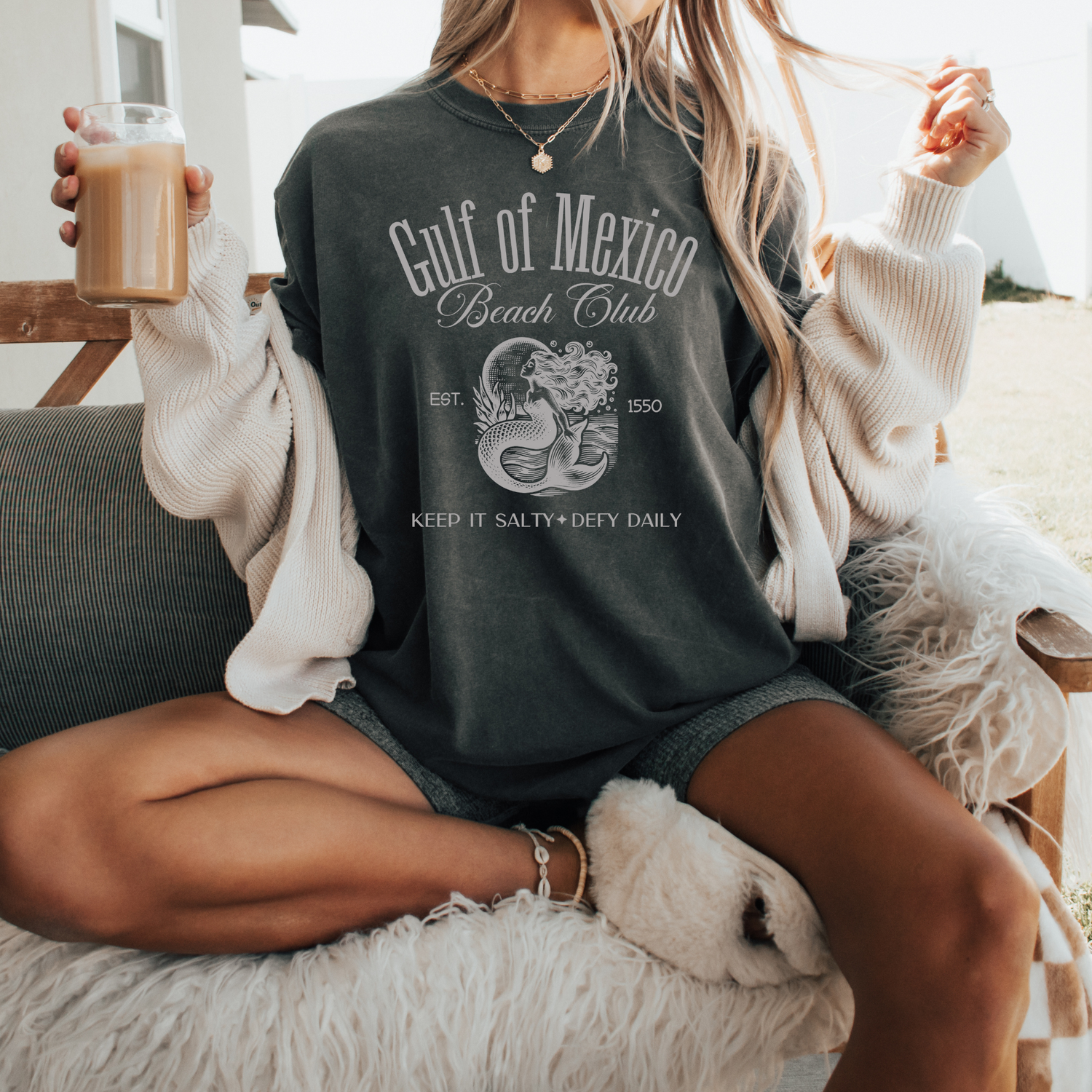 Woman wearing Gulf Of Mexico Beach Club Est 1550 Comfort Colors® Shirt Sweatshirt sitting outdoors with coffee in hand