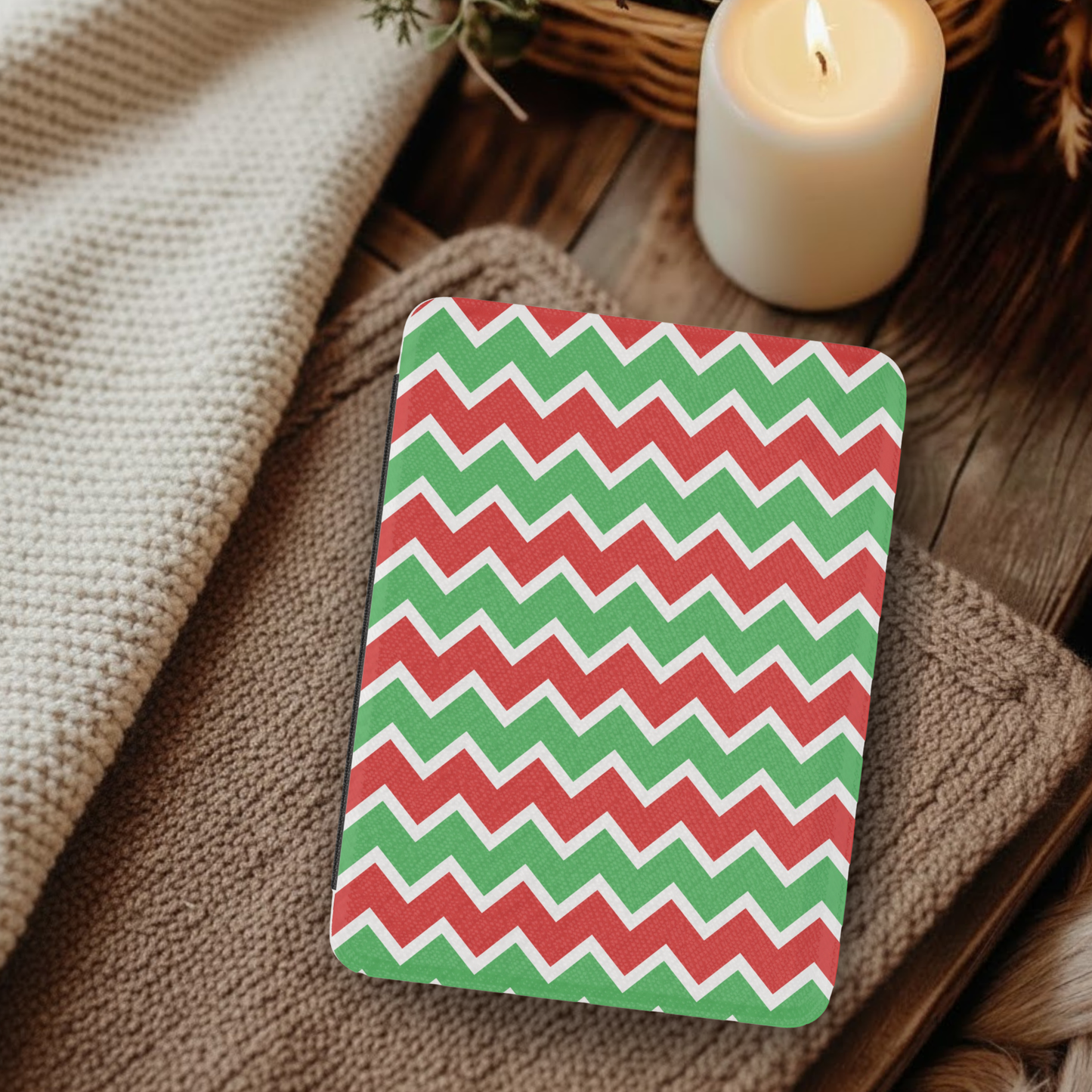 Christmas Chevron Pattern Leather Kindle Case with Hand Strap resting on cozy fabric near a lit candle and woven basket background.