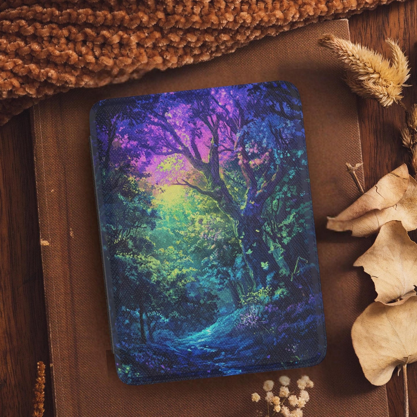 Colorful Magic Forest Leather Kindle Case with Hand Strap featuring vibrant forest artwork on a wooden surface with dried leaves