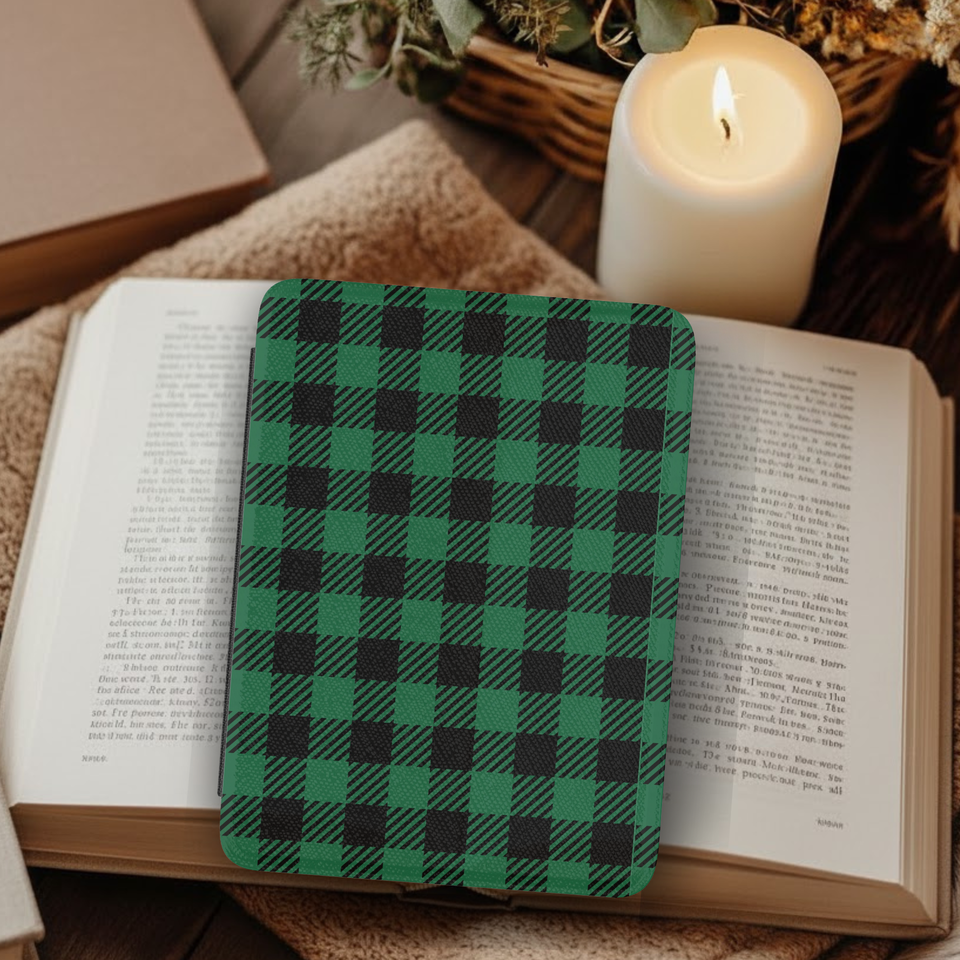 Green Buffalo Plaid Leather Kindle Case with Hand Strap resting on an open book near a lit candle