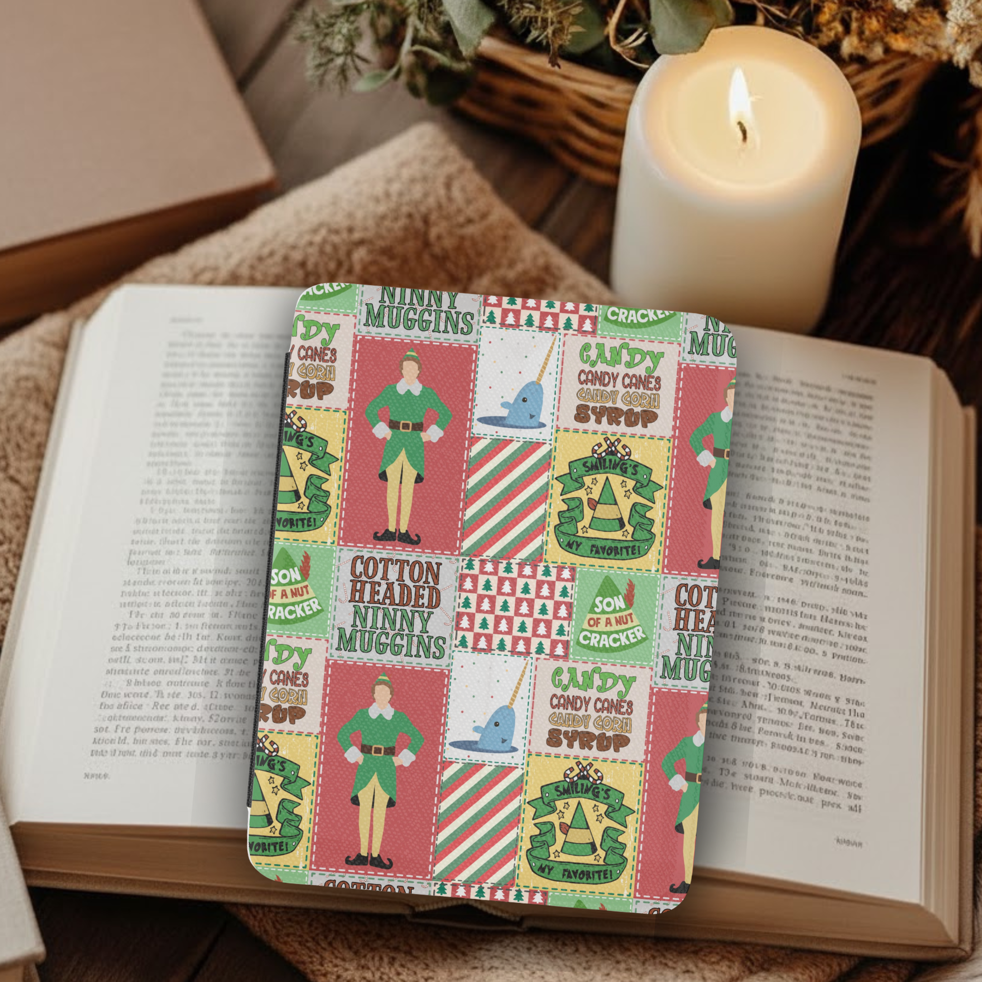 Christmas Elf Patchwork Leather Kindle Case with Hand Strap resting on an open book near a lit candle in a cozy setting