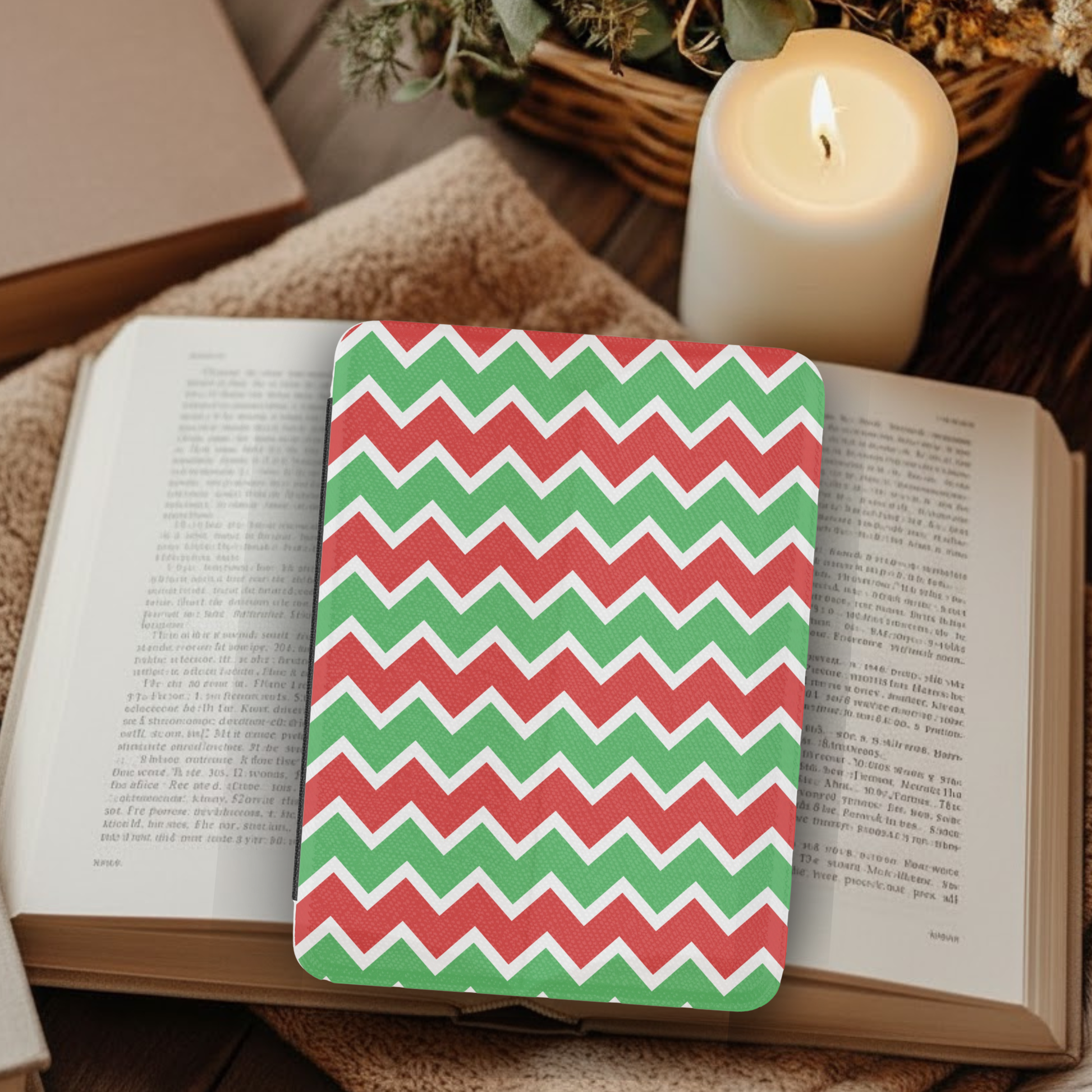 Christmas Chevron Pattern Leather Kindle Case with Hand Strap resting on an open book beside a lit candle and cozy decor