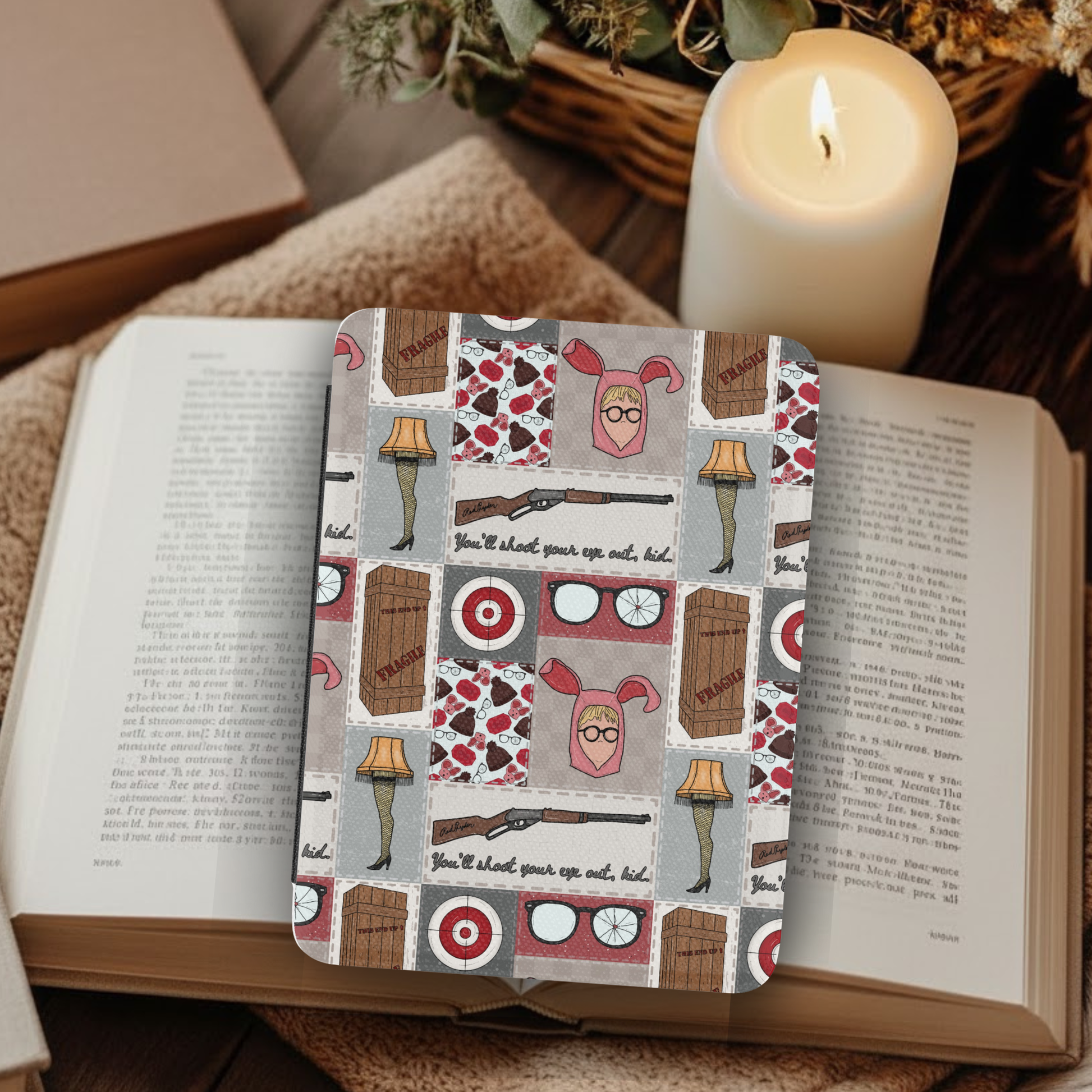 A Christmas Story Patchwork Leather Kindle Case with Hand Strap displayed on an open book with a lit candle nearby