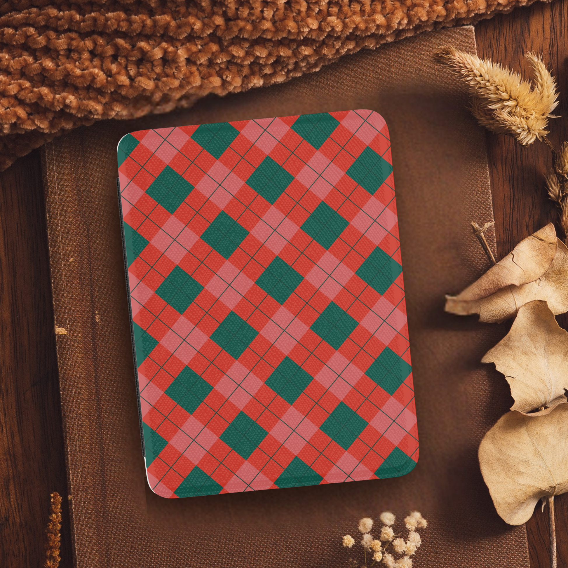 Classic Christmas Plaid Leather Kindle Case with Hand Strap resting on fabric with autumn leaves and cozy textures nearby