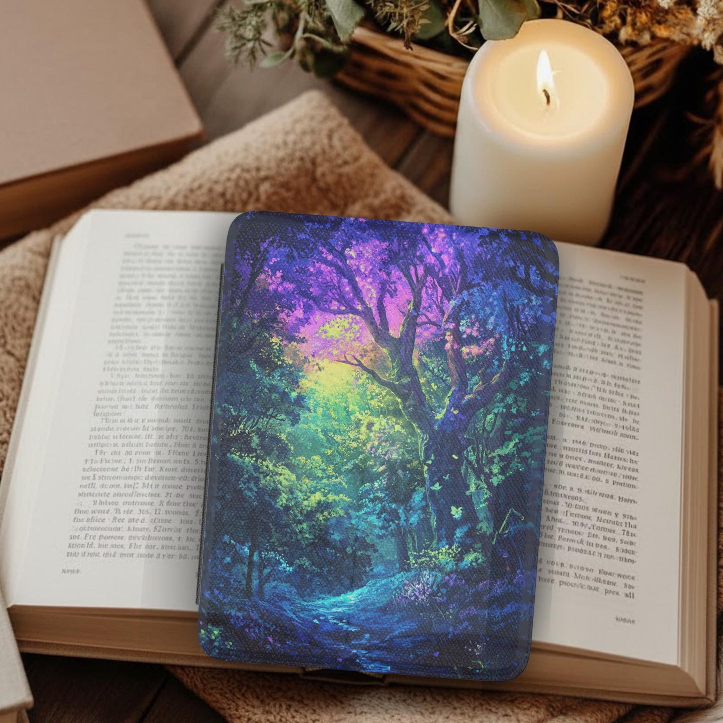 Colorful Magic Forest Leather Kindle Case with Hand Strap resting on an open book beside a lit candle in cozy setting
